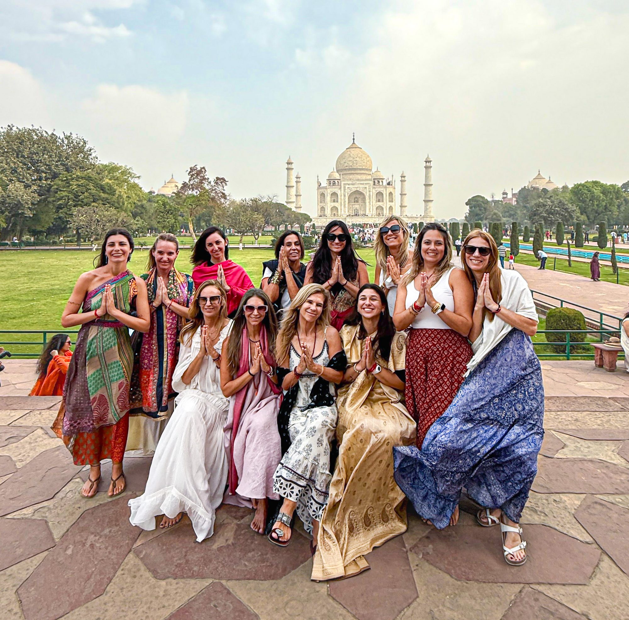 Grupo de viajeras latinoamericanas saludando con las manos juntas frente al Taj Mahal en Agra