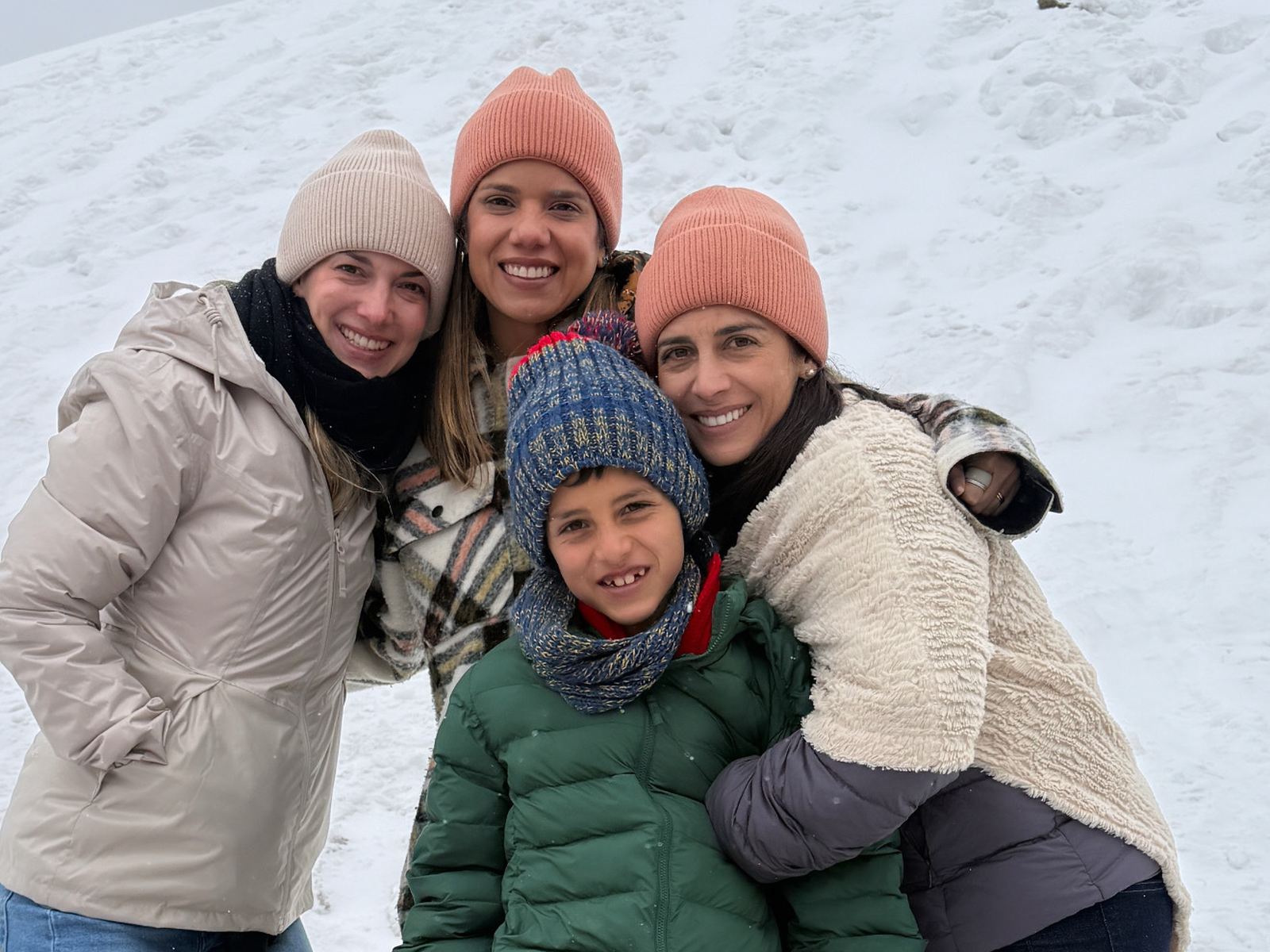Un niño con gorro de lana y bufanda sostiene una bola de nieve mientras tres mujeres lo abrazan, sobre la nieve del puerto de Khardung La, en Ladakh, India.