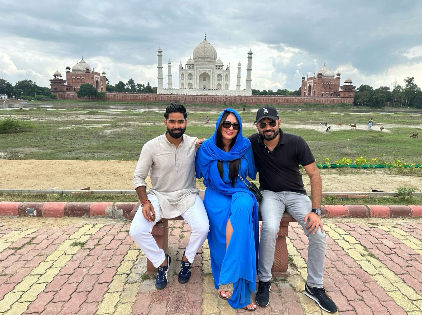 Tres personas sentadas en un banco con el Taj Mahal al fondo, desde la orilla opuesta del río Yamuna, en Agra