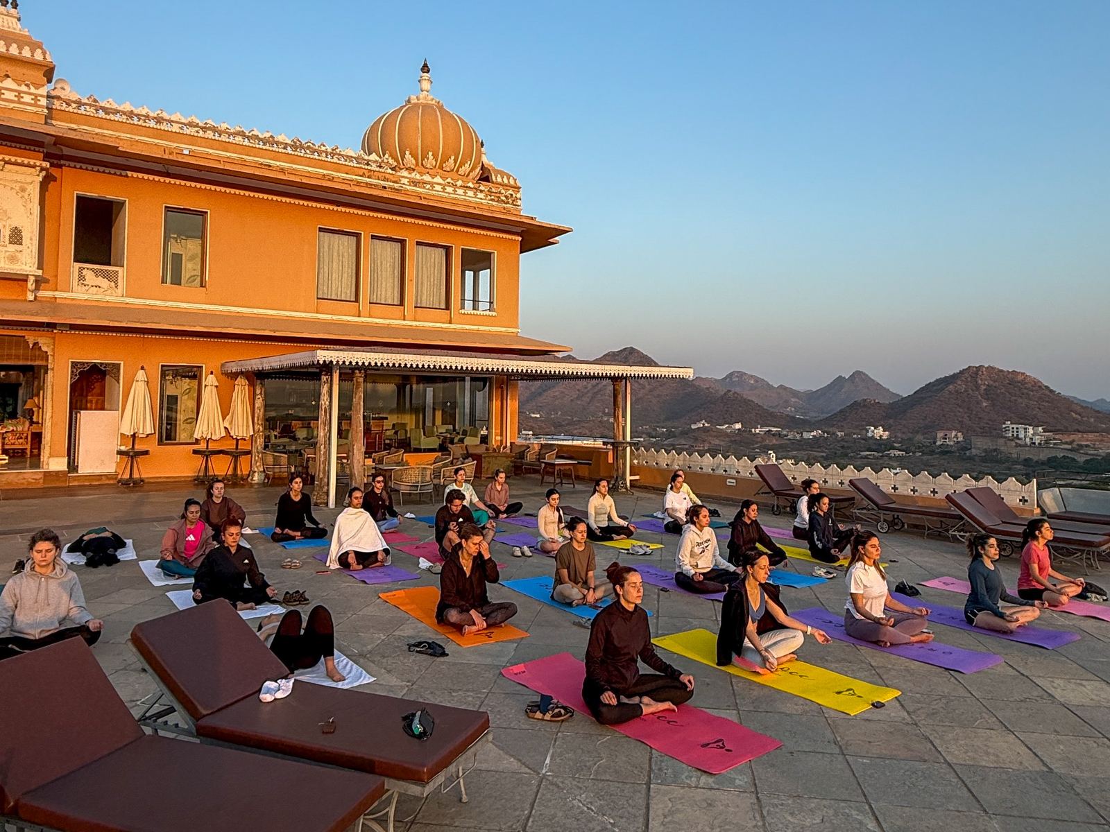Grupo practicando yoga y meditacion al amanecer en la terraza de un palacio en la India
