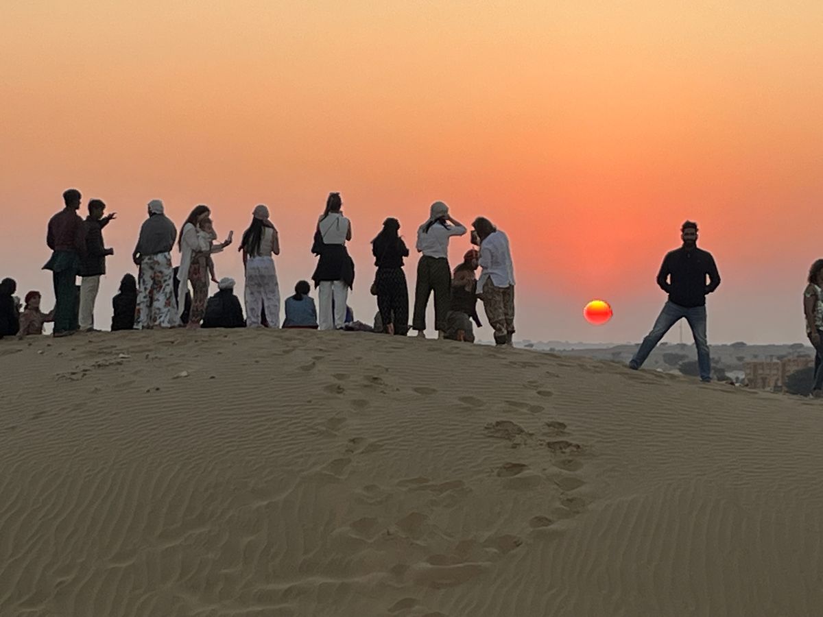 Siluetas de viajeros sobre una duna del desierto del Thar mientras el sol se pone en el horizonte