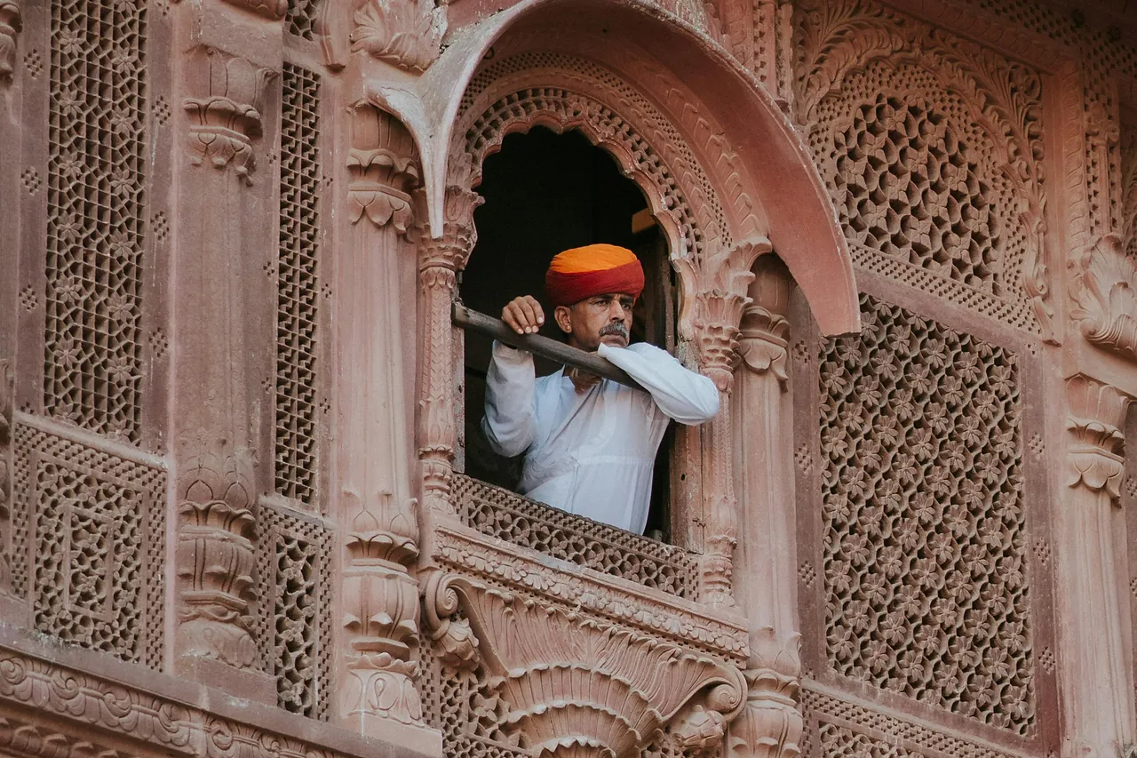 Hombre con turbante naranja asomado a un balcón de arenisca tallada del fuerte de Mehrangarh