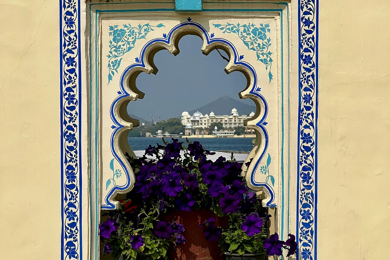 Ventana con marco pintado de azul que enmarca el lago Pichola y sus palacios, en Udaipur