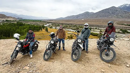Cuatro viajeros posan con sus motos Royal Enfield sobre un valle de Ladakh, con montañas nevadas al fondo
