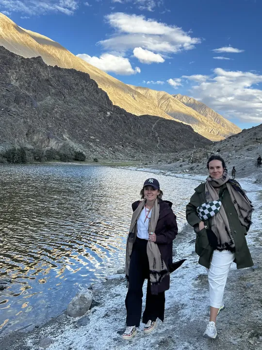 Dos viajeras a la orilla de un lago de montaña bajo picos áridos, en Ladakh